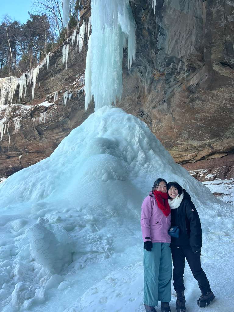two girls hugging, standing in front of a frozen waterfall